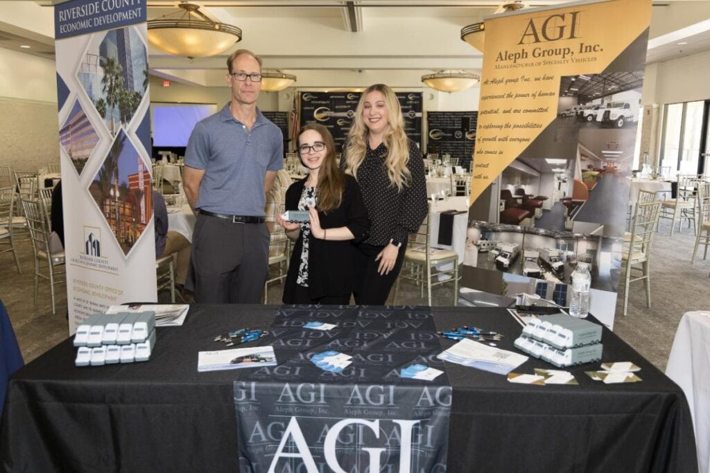 AGI staff posing with award behind the booth at the Inland Empire World Trade Conference.